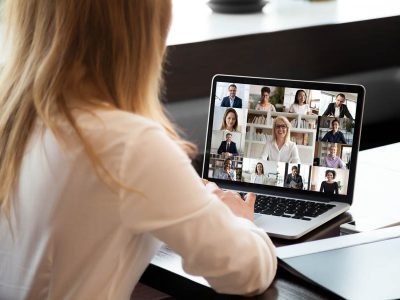Businesspeople communicating using application webcam laptop view over businesswoman shoulder View over businesswoman shoulder sit at workplace desk looks at pc screen during group videocall with different age and ethnicity colleagues using application and webcam, distant communication concept