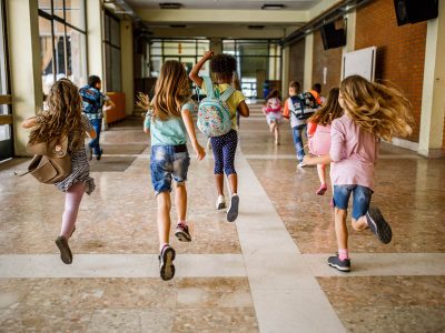 Rear view of group of school children running down the hallway. Back view of elementary students running in the school hallway.