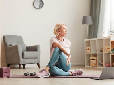 Senior woman sitting on the floor on exercise mat in front of laptop and training at home