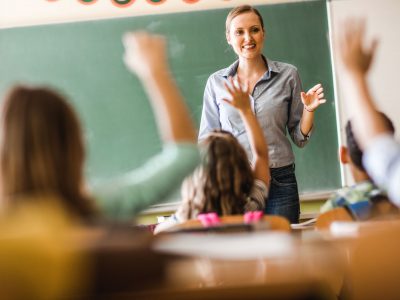 Happy elementary teacher asked a question on a class at school. Happy female teacher asked a question during a class at elementary school.