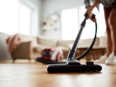 Close-up of unrecognizable woman using modern powerful hoover while vacuuming floor at home