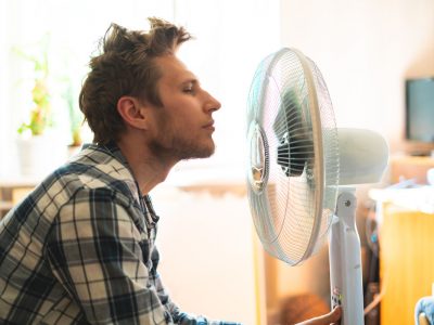 person enjoying the electric fan, cooling his face at home, during summer heat