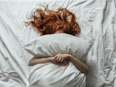 Red-haired little girl wakes up in the morning in her crib with white bed linen.