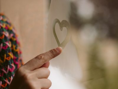 Beautiful girl hand drawing hearts in the window. Love and solitude concept.