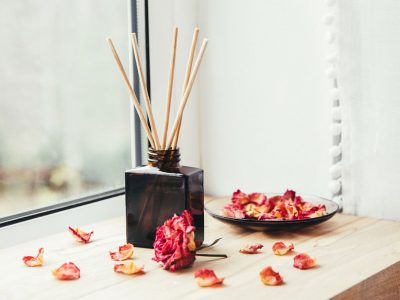 Brown glass bottle container with wood stick diffusers on home wooden window sill with beautiful dry pink rose petals for decoration. Minimalist air freshener concept.