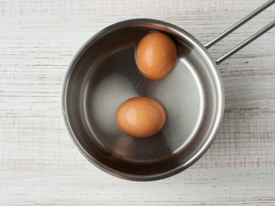Two eggs in the water in a metal pan on the table  top view