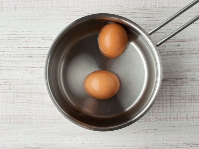 Eggs in water in a metal pan top view Two eggs in the water in a metal pan on the table top view
