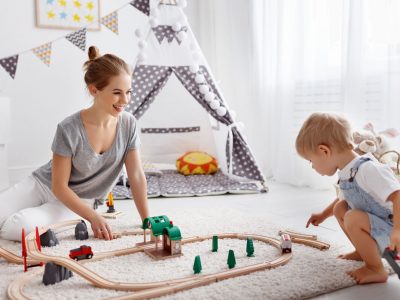 happy family mother and child son playing together in toy railway in playroom